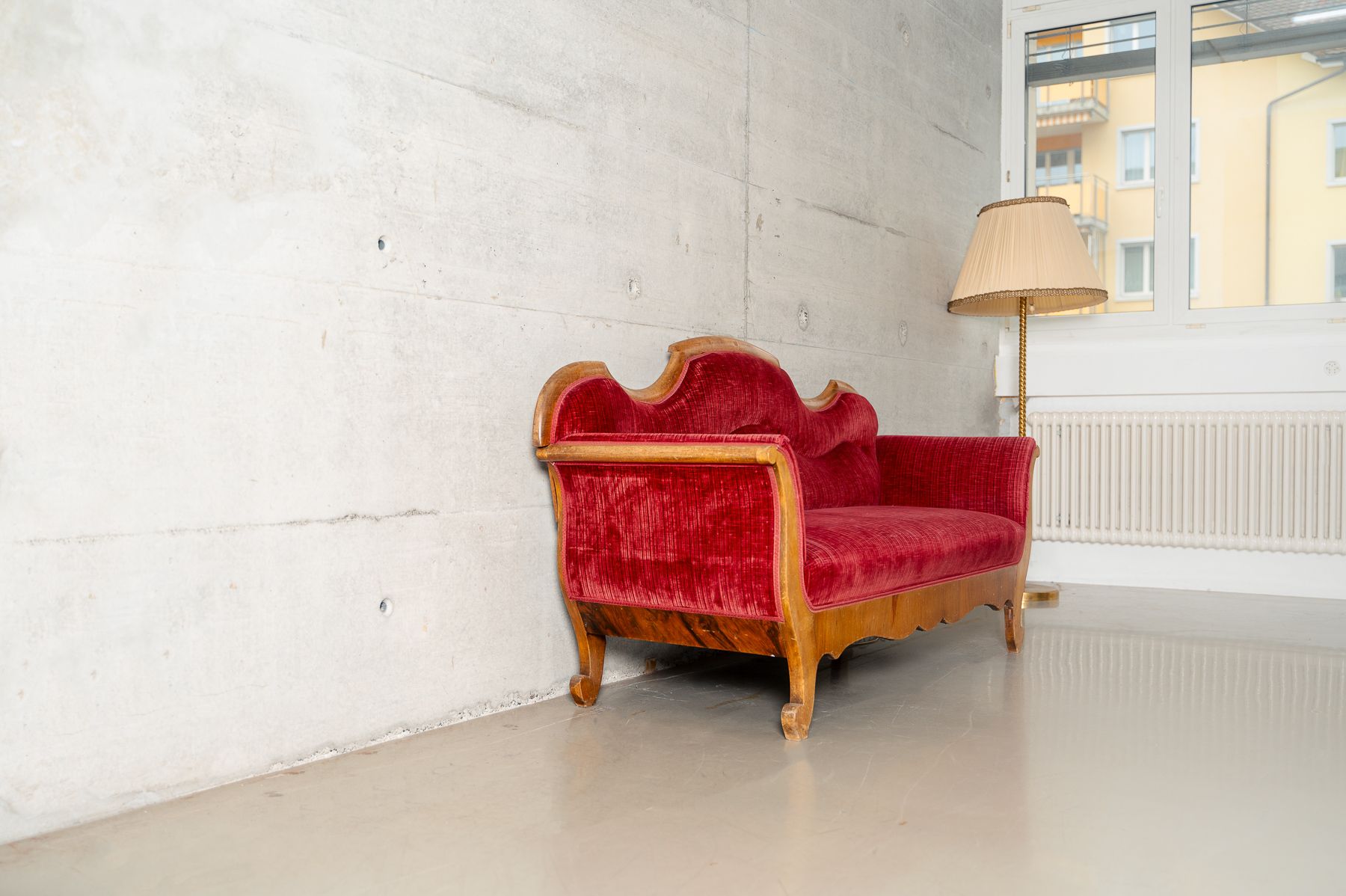 Rotes Samtsofa vor heller Betonwand im Fotostudio
